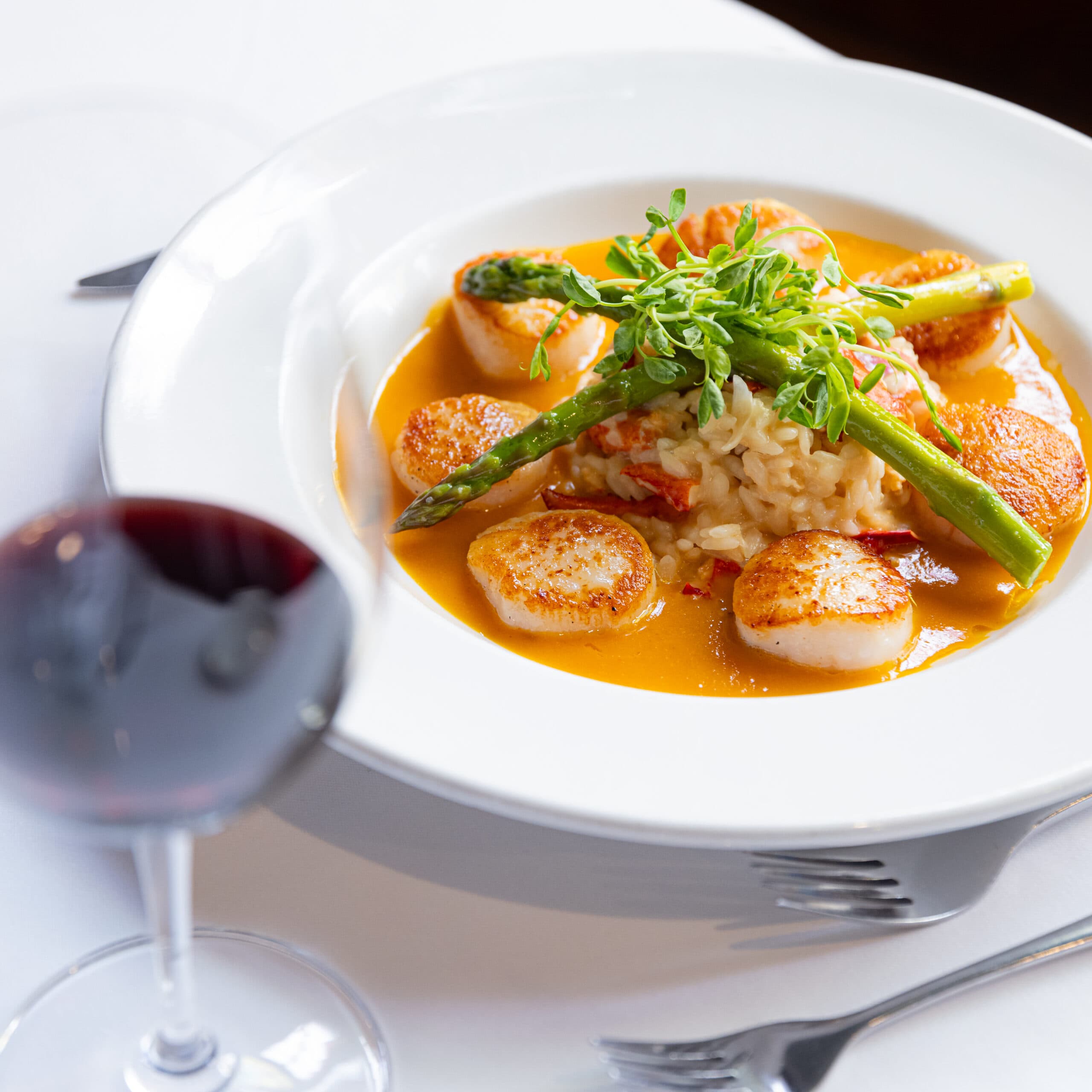 glass of red wine and scallops in dish with sauce topped with asparagus