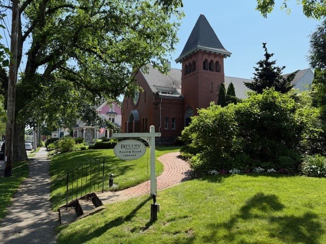A red brick building with a tower, surrounded by greenery and a sign for Belfry Food & Drink.
