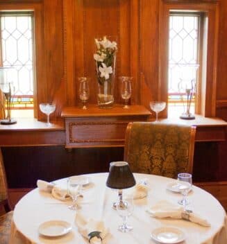 round table set with linen tablecover in a formal dining room situated in front of two windows