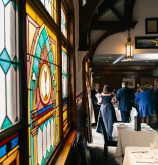 large colorful stained glass window to the left with a bridesmaid and groomsman waiting to have their photo taken in the background